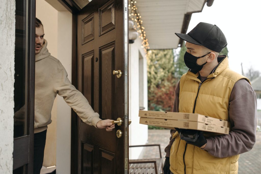 delivery driver delivering pizza to customer in mask