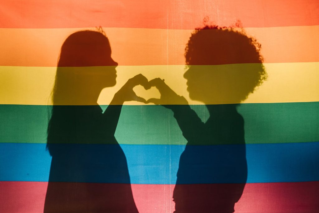 shadow of people making a heart together on a pride flag