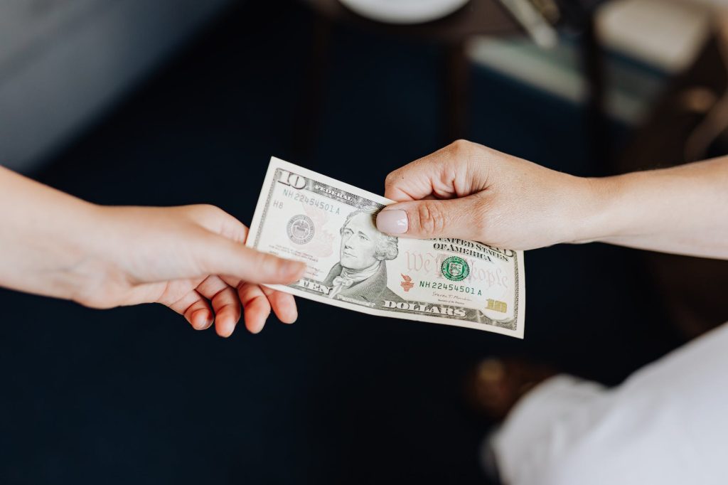 customer hands money to worker, tipping them a ten dollar bill