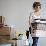 concentrated woman carrying stack of cardboard boxes for relocation